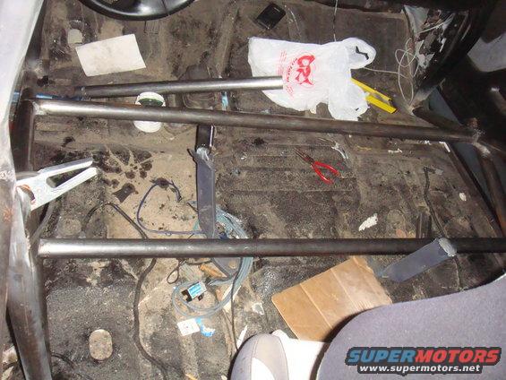 Interior of a vehicle with a roll cage installed. Floor is dirty with tools and a plastic bag