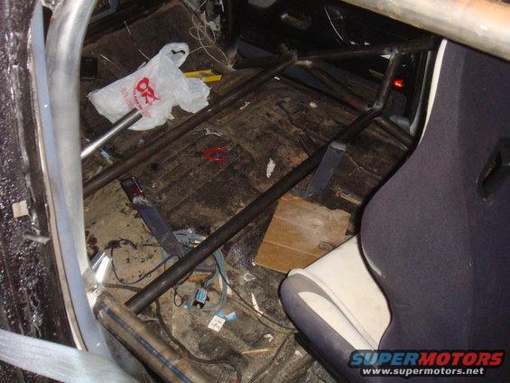 Interior view of a vehicle with a roll cage, racing seat, and debris on the floor