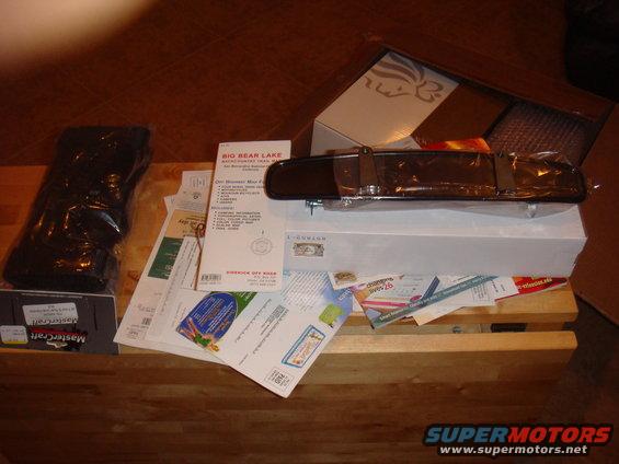 Automotive rearview mirror in packaging, with various documents and a black item in plastic