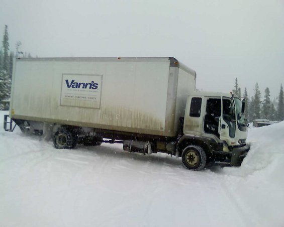 Box truck with Vann's logo stuck in deep snow, trees in background