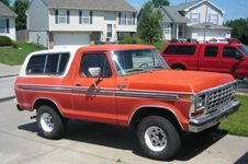 Orange 1978 Ford Bronco with white removable top, chrome trim, and white wheels parked on driveway