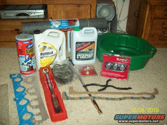 Automotive parts including oil, antifreeze, gaskets, a torque wrench, and gauges laid out on a carpeted floor