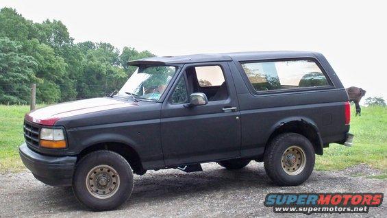 Black Ford Bronco parked on a dirt road with trees in the background