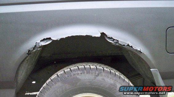 Rusted rear wheel well on a dark vehicle
