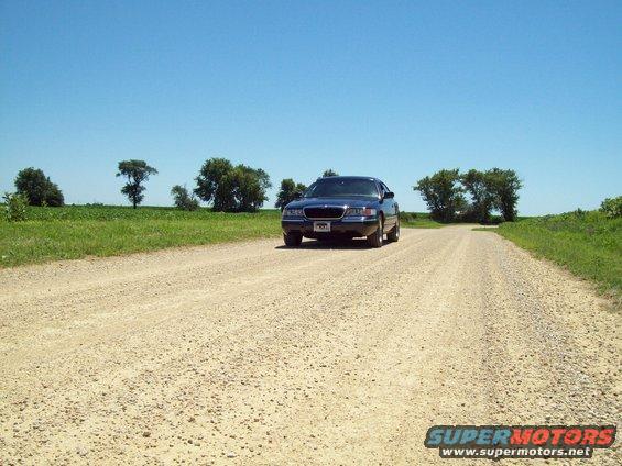 Dark blue sedan on a gravel road, front view. Visible grille and headlights