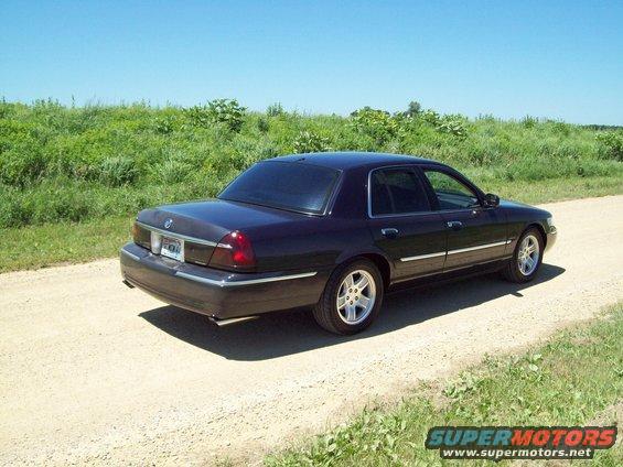 Dark sedan parked on dirt road with grassy field behind it. License plate visible