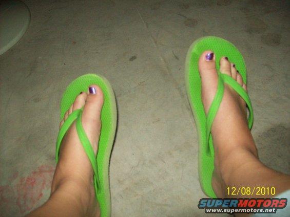 Feet in green flip-flops with purple nail polish