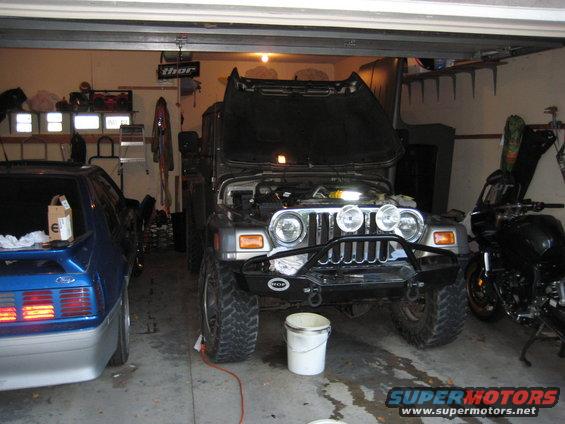 2005 Jeep Wrangler with hood open, parked next to a blue Ford Mustang and a black motorcycle in a garage