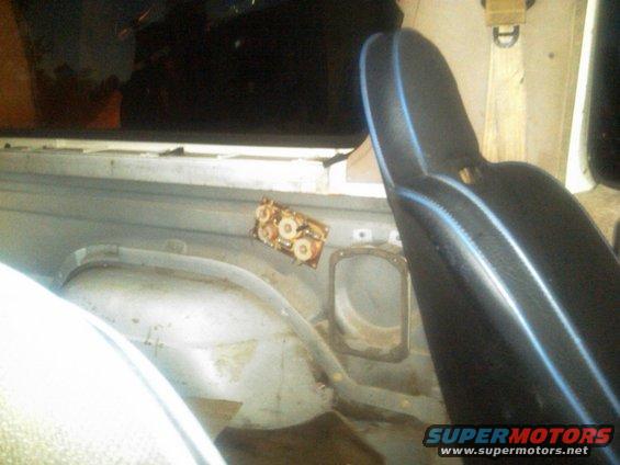 Vehicle interior with black seat and blue trim, showing exposed metal and a small electrical component