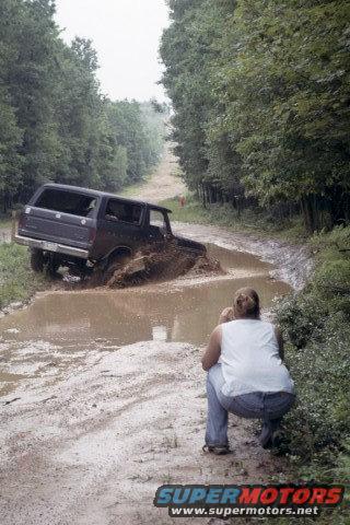 1979 Ford Bronco II stuck in a mud puddle on a dirt road, person crouching nearby