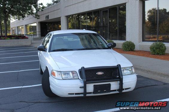 White Ford Crown Victoria police car with a push bar parked in front of a building