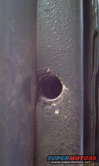 Close-up of a dark, textured metal frame with a circular hole and some white debris