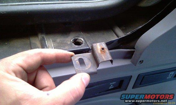 Hand holding rusty metal bracket near gray dashboard with 'PUSH' labels