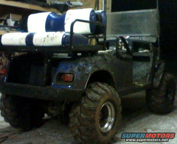 Modified golf cart with large tires, carrying blue and white barrels on a rack