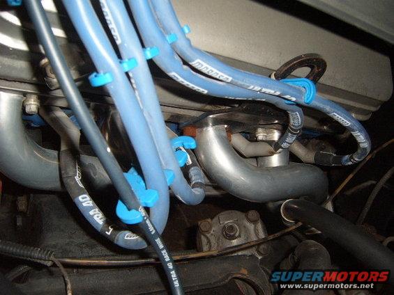 Close-up of blue spark plug wires and exhaust manifold in an engine bay. Some wires have text like 'ULTRA 40 RACE WIRE'