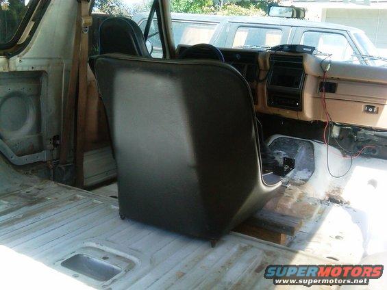Interior of a disassembled vehicle, showing a dark seat and dashboard. Another vehicle is visible outside