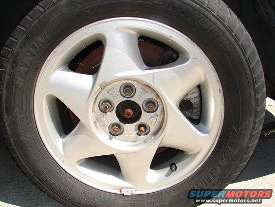 Silver five-spoke alloy wheel with a black tire, showing brake components and lug nuts