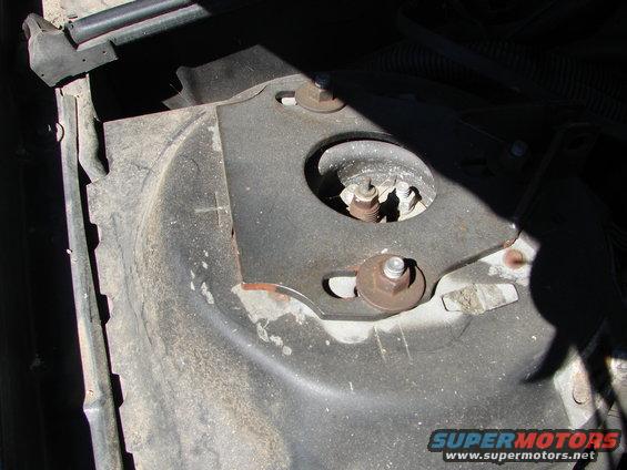 Close-up of a vehicle's strut mount area with bolts and metal plate