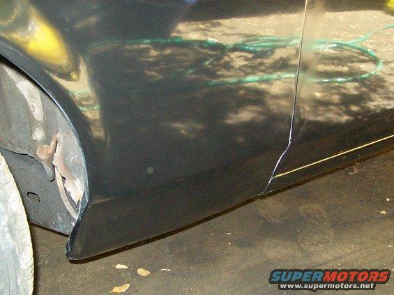 Black car body panel with visible damage and repair lines near the wheel well