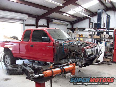 Red pickup truck with front end removed, in a garage