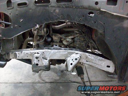 Front frame and engine bay of a vehicle undergoing repair. Shows suspension and engine parts