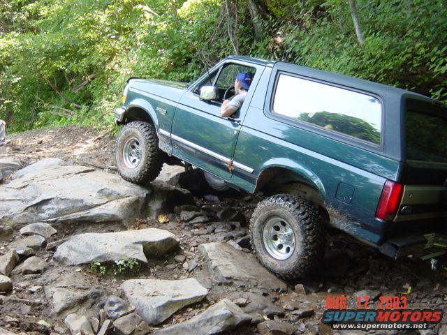 Green Ford Bronco navigating a rocky, muddy trail, driver visible
