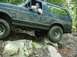 1995 Ford Bronco - A 1995 Ford Bronco navigates a rocky path in a wooded area, with a driver visible behind the wheel.