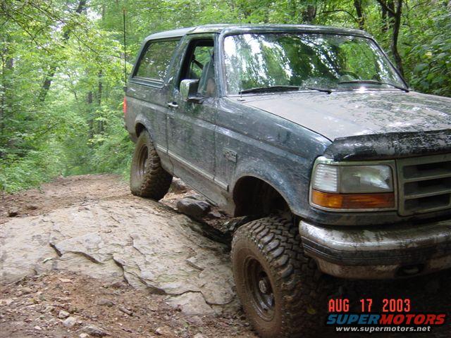 Dark green Ford Bronco on a rocky trail, front 3/4 view. Mud-splattered with off-road tires