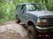 1995 Ford Bronco - A Ford Bronco navigates a challenging, rocky off-road path surrounded by dense forest.