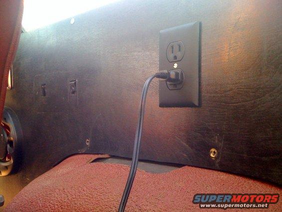 Interior electrical outlet with a plug inserted into it. Carpeted floor is visible below
