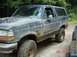 1995 Ford Bronco - This 1995 Ford Bronco is covered in mud, suggesting it has been used off-road. Another vehicle is partially visible to the right.