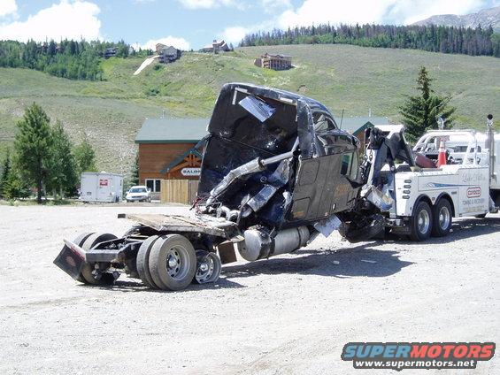 Towed semi-truck with severe front-end damage, being loaded onto a tow truck
