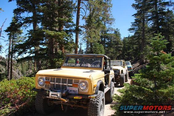 Yellow Ford Bronco on a dirt road with other vehicles behind it