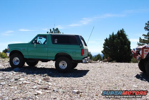 Green SUV parked on a rocky surface, side view. It has large tires and a lifted suspension