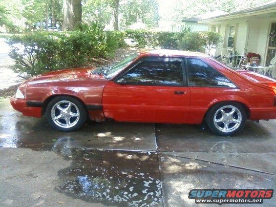 1989 Ford Mustang coupe, red paint, chrome five-spoke wheels, parked on wet concrete