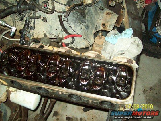 Engine valve train with oil visible inside the cylinder head. Some tools and rags are in the background