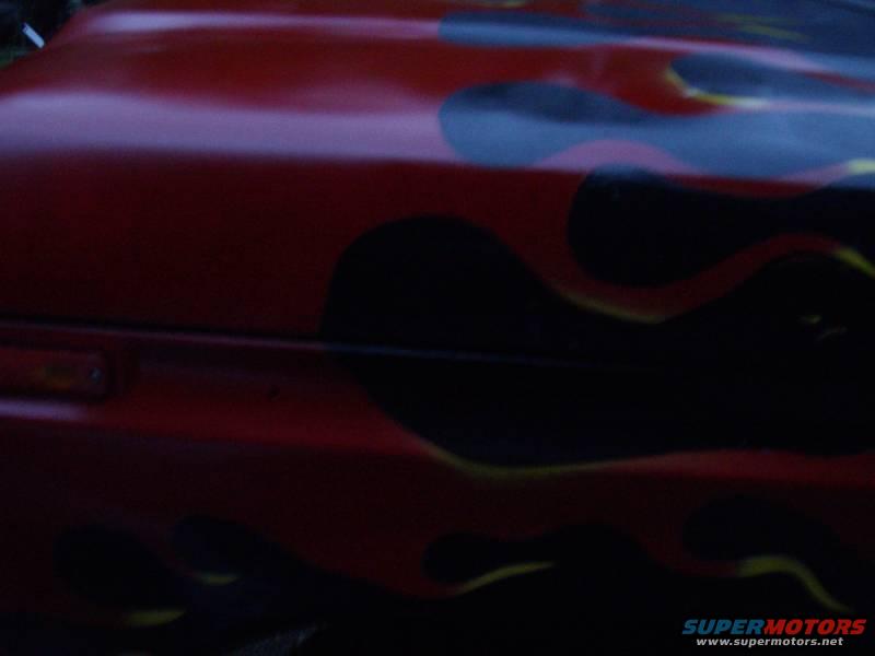 Red car hood with flame graphics. A small orange marker light is visible on the left