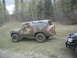 1985 Ford Bronco - Mud-covered Ford Bronco with camouflage paint parked in a wooded area.
