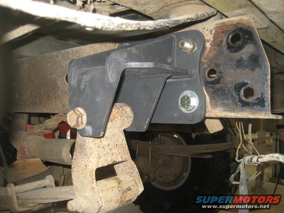 Close-up of a black suspension bracket bolted to a rusty frame, with leaf springs visible
