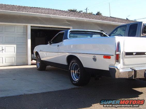 White coupe utility parked in front of a garage, with a gray pickup truck partially visible inside