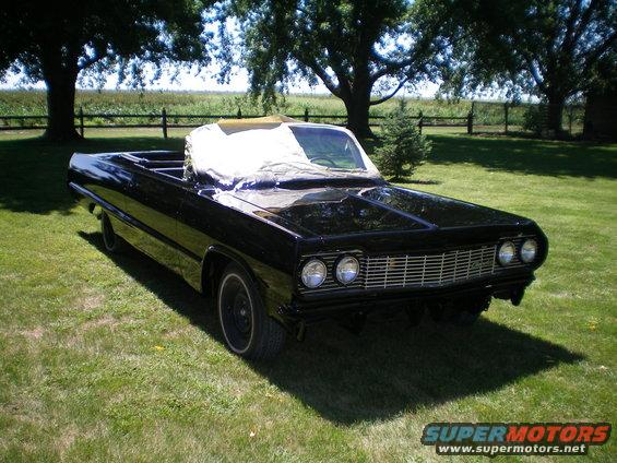Black 1964 Chevrolet Impala convertible with a tarp covering the top, parked on grass