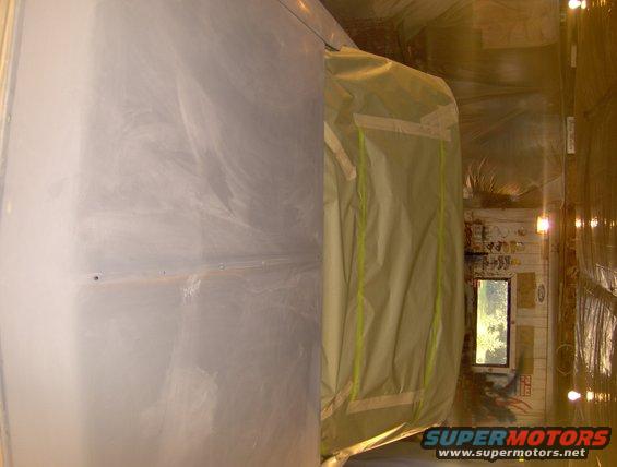 car body covered in primer, taped off for painting inside a booth