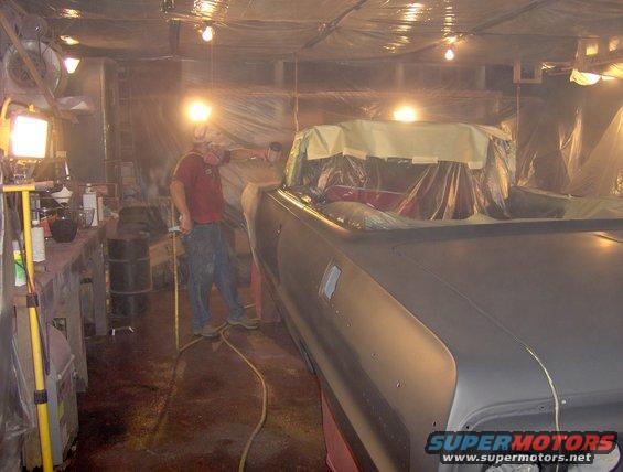 Car body covered in plastic sheeting, being prepped for paint in a workshop with lights and equipment