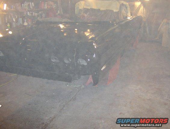 Car body on jack stands in a garage, covered in dust. The front end has four headlights