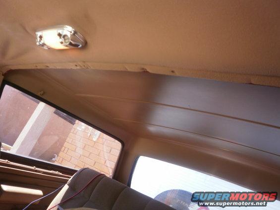 Interior view of a car's headliner with a dome light and a window showing a brick building