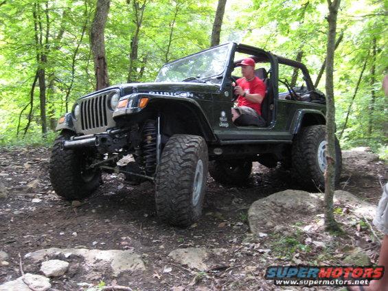 Black Jeep Wrangler Rubicon on rocky trail, driver in red shirt and hat