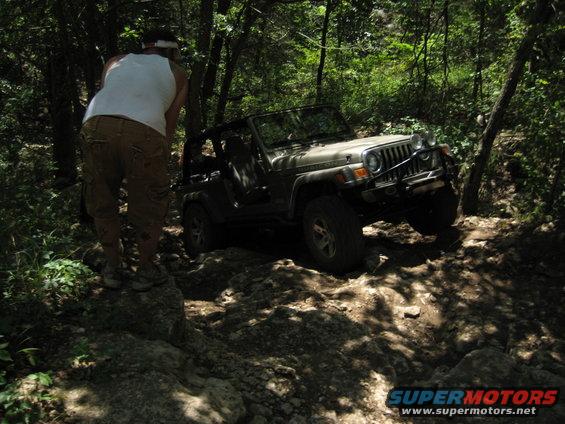 Tan Jeep Wrangler navigating rocky terrain, front-right tire elevated