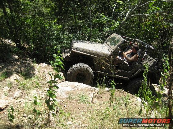 muddy Jeep TJ climbing rocky trail, driver visible