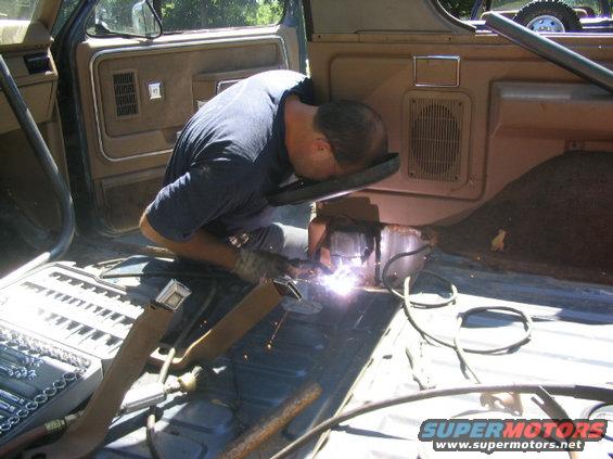 Man welding inside a brown interior of an older SUV, sparks flying