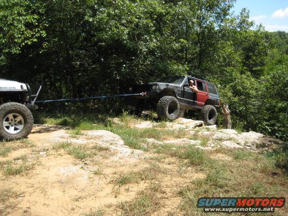 Black Jeep Cherokee XJ with red rear doors being towed by a white Jeep Rubicon on a rocky trail